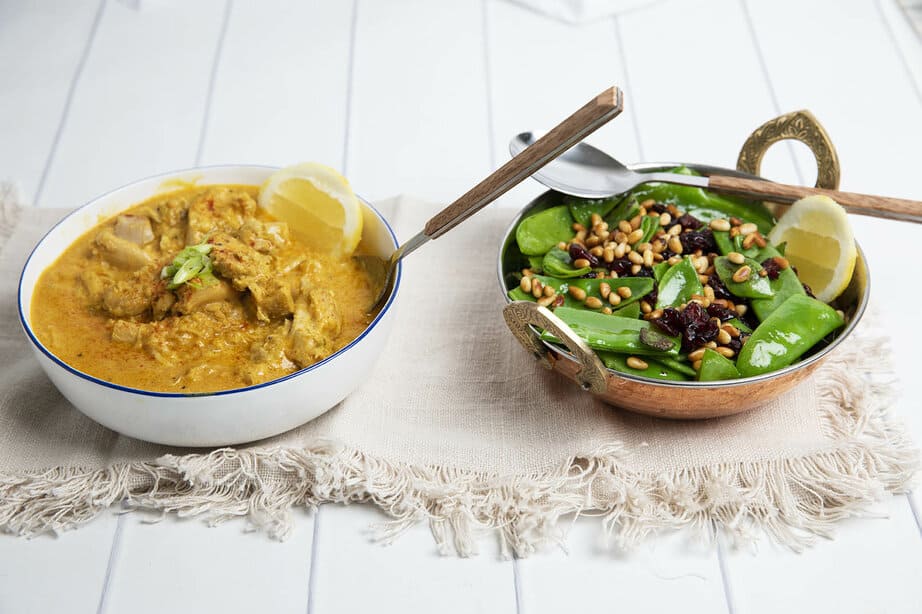 Moroccan Chicken dish beside a snow pea side on a white background