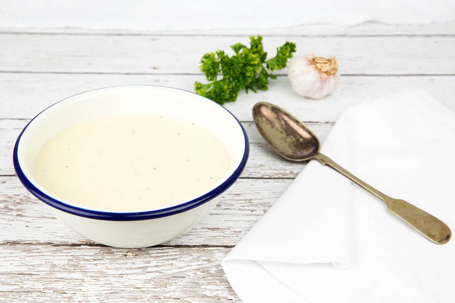 Creamy Garlic Sauce Recipe in a white enamel bowl on a wooden background with napkin and spoon