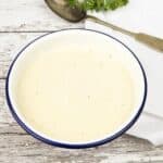 Long Pin image of a bowl of garlic cream sauce on a wooden background