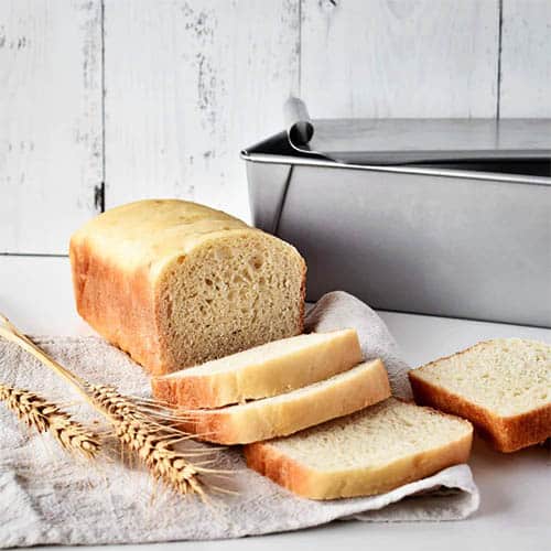 Thermomix Jumbo Bread tin with a loaf of sliced bread beside it on a tea towel