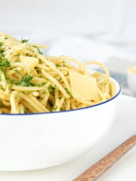 Thermomix Boiled spaghetti pasta in a white bowl on a white background with parsley and cheese on top.