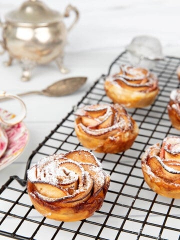 Apple Rose Pastry on a black wire cooling rack with a sugar bowl and tea cup.