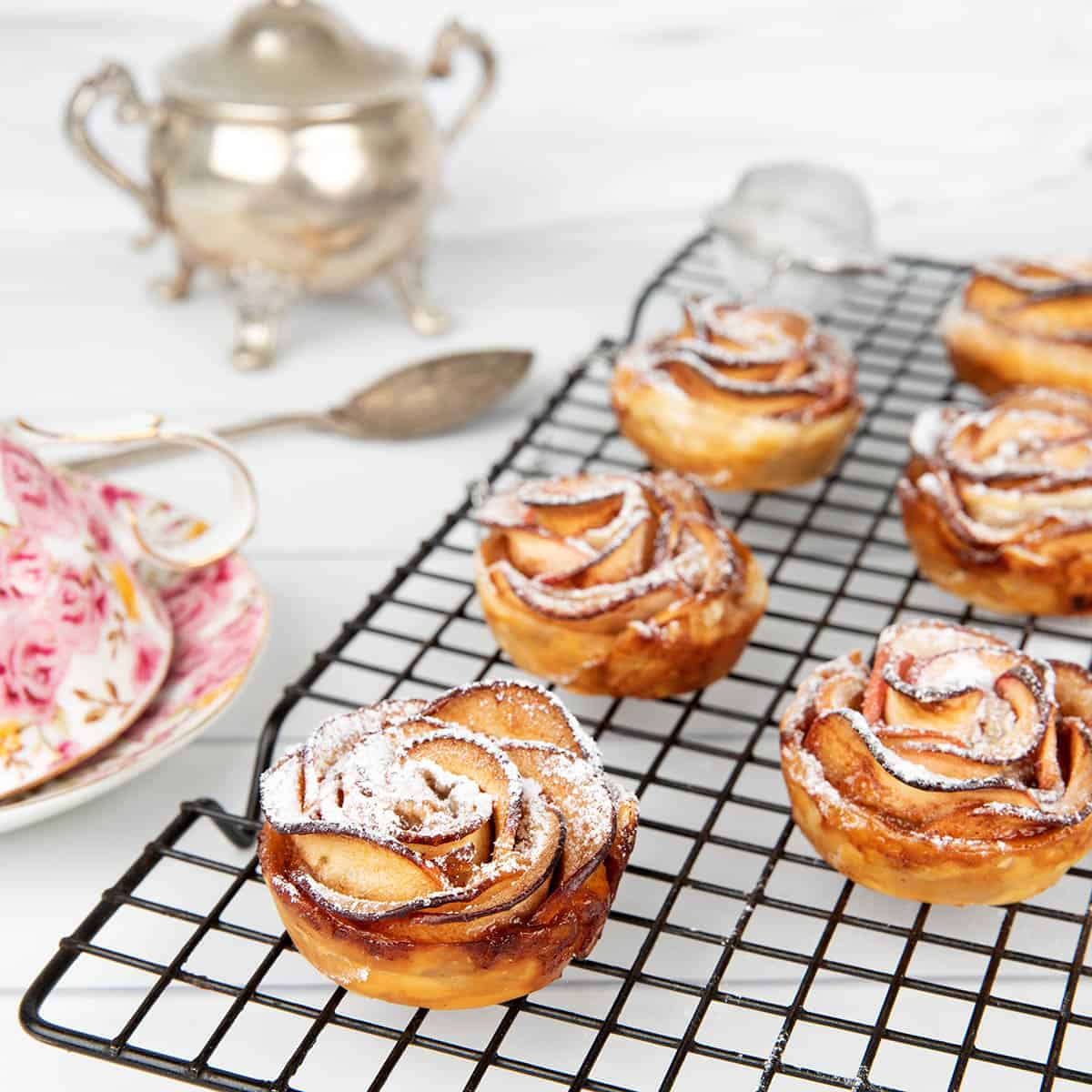Apple Rose Pastry on a black wire cooling rack with a sugar bowl and tea cup.