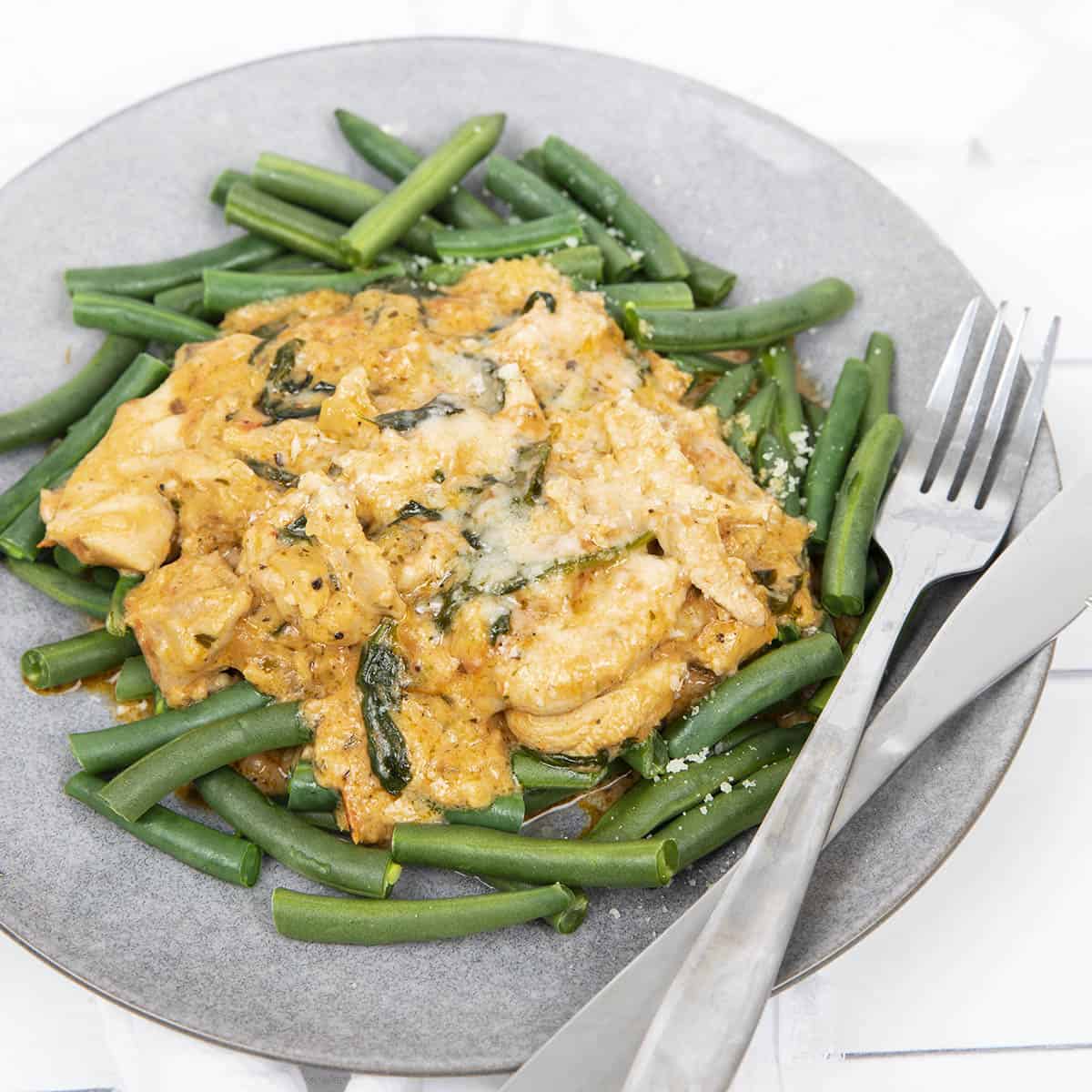 Tuscan Chicken served on a bed of green beans on a grey plate