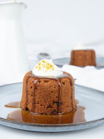 Sticky date pudding with caramel sauce with cream and orange zest on white background