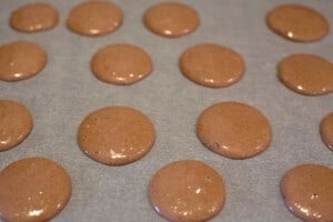 Chocolate Macarons pipes onto baking paper.