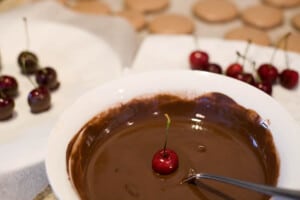 Dipping cherries in chocolate mixture for coating.
