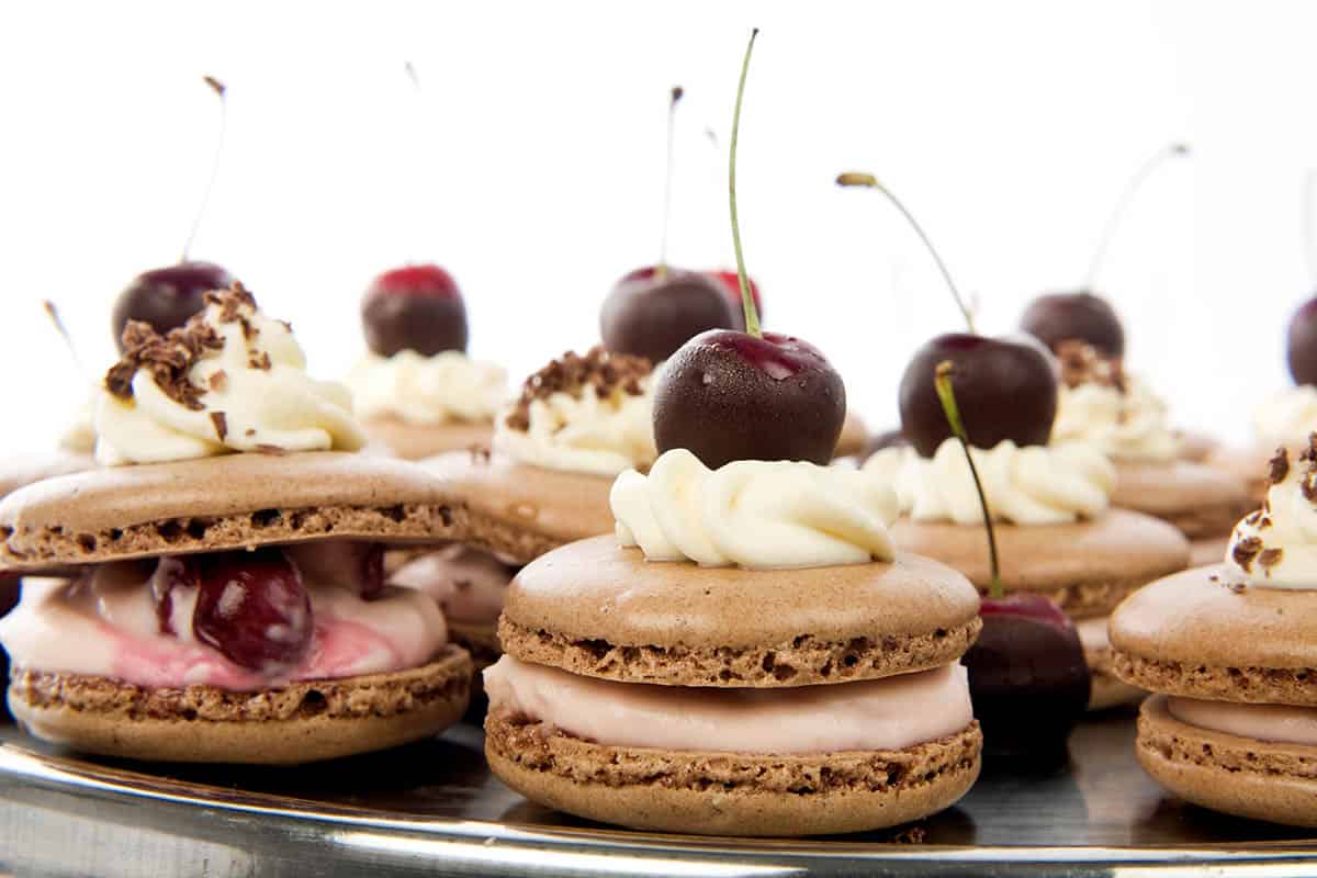 Silver platter of chocolate Thermomix macarons with cream and cherries on top.