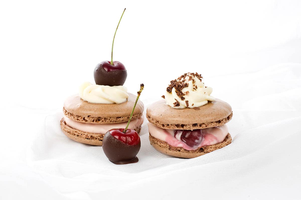 Two Chocolate Thermomix macarons on a white background with cherries on top
