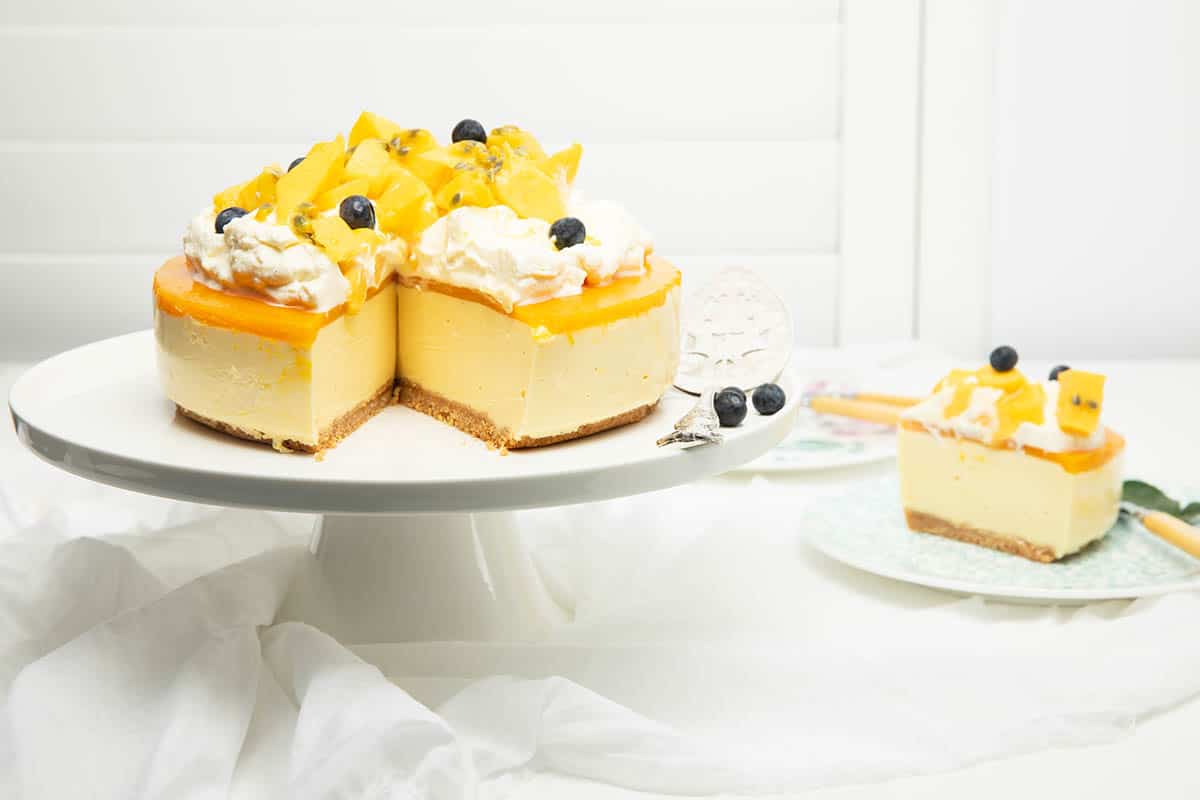 Mango cheesecake with a slice taken out and displayed on a plate.