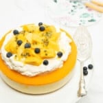 Whole Thermomix Mango Cheesecake Layered with cream and fruit on top, white background.