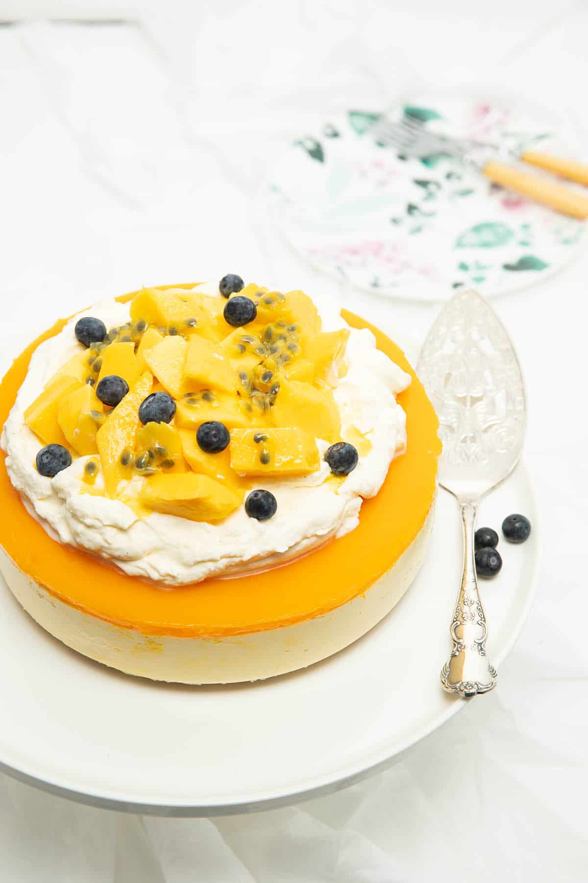 Whole Thermomix Mango Cheesecake Layered with cream and fruit on top, white background.