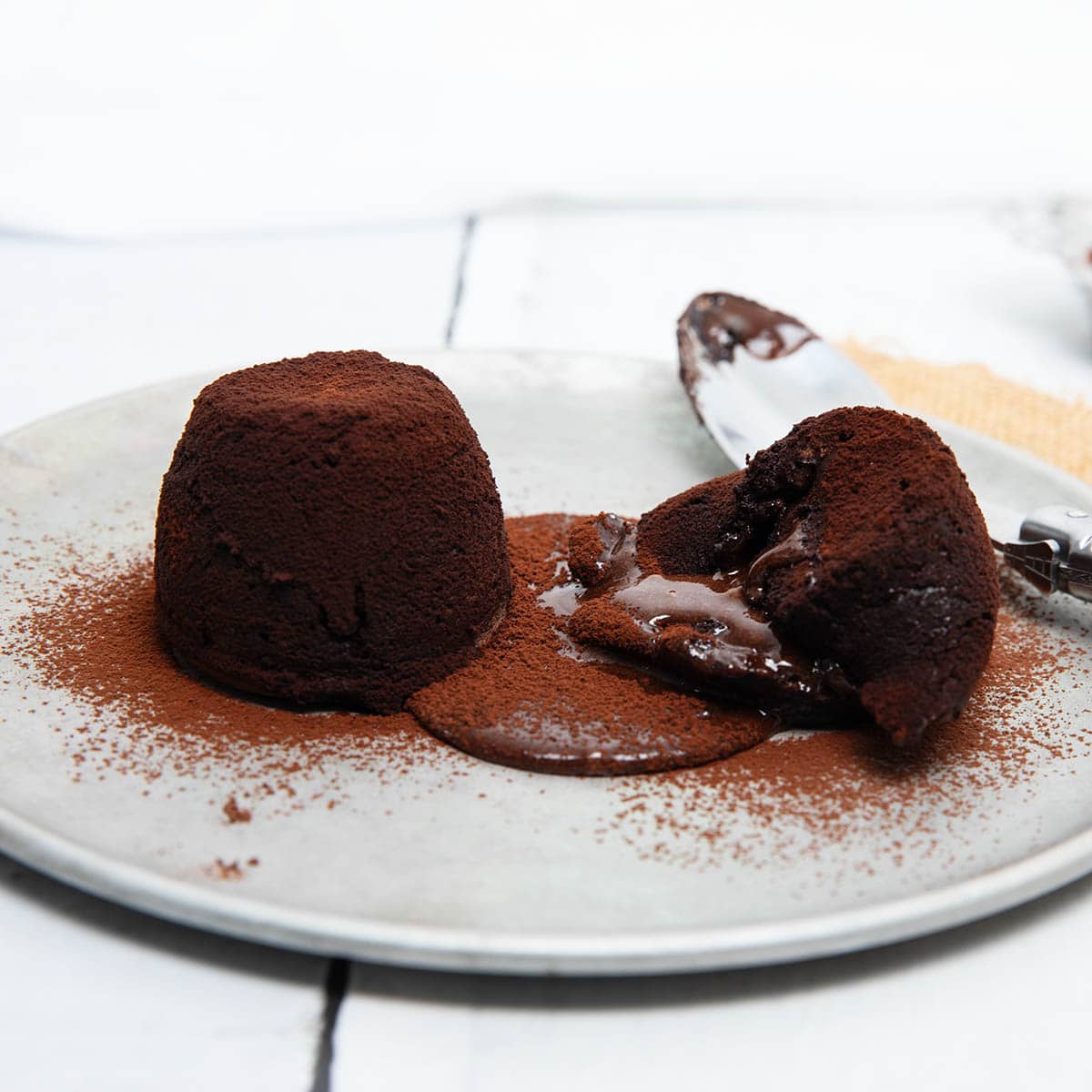 Two Chocolate Fondant Cakes close up with a spoon squashing chocolate sauce out.
