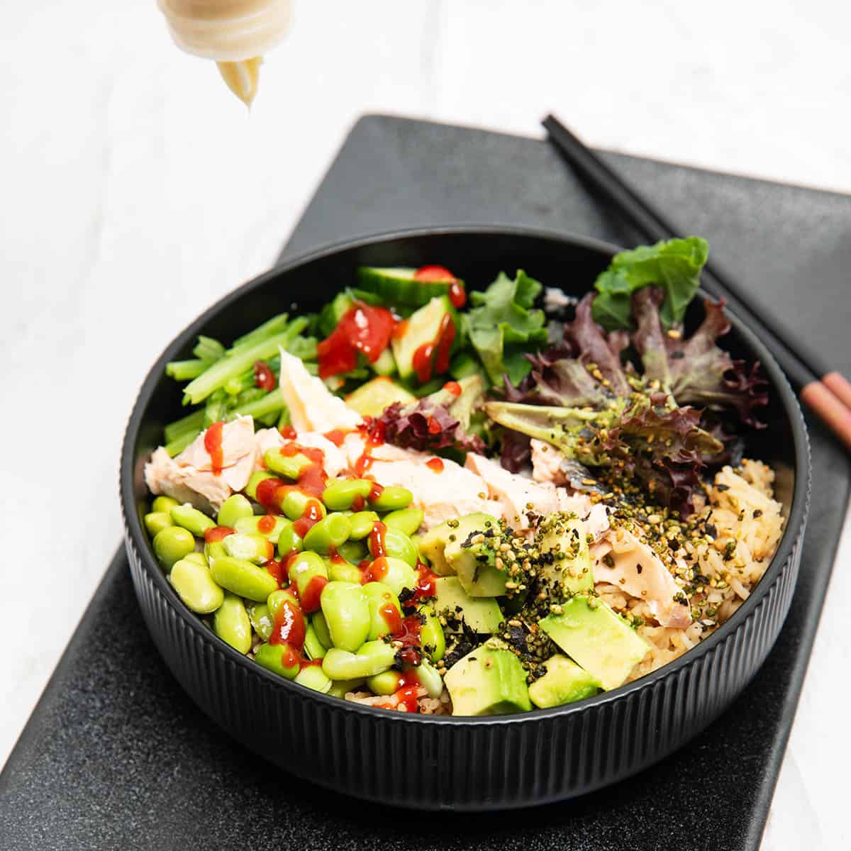 Thermomix Teriyaki Salmon bowl with edamame beans lettuce and advocado sitting on rice in a black bowl.
