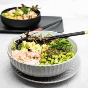 Teriyaki Salmon bowl on white background with edamame beans and avocado, rice and lettuce in the bowl.