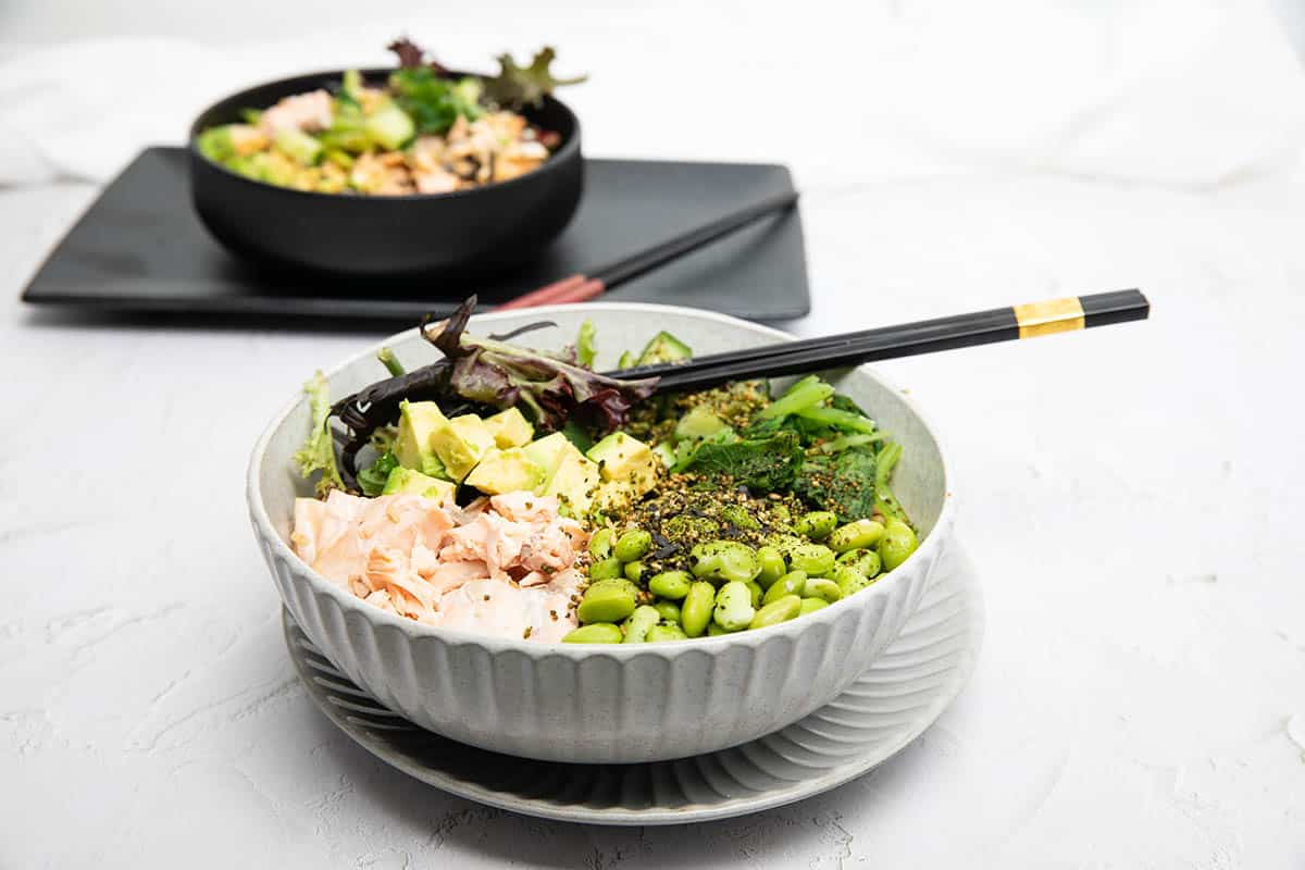 Teriyaki Salmon bowl on white background with edamame beans and avocado, rice and lettuce in the bowl.