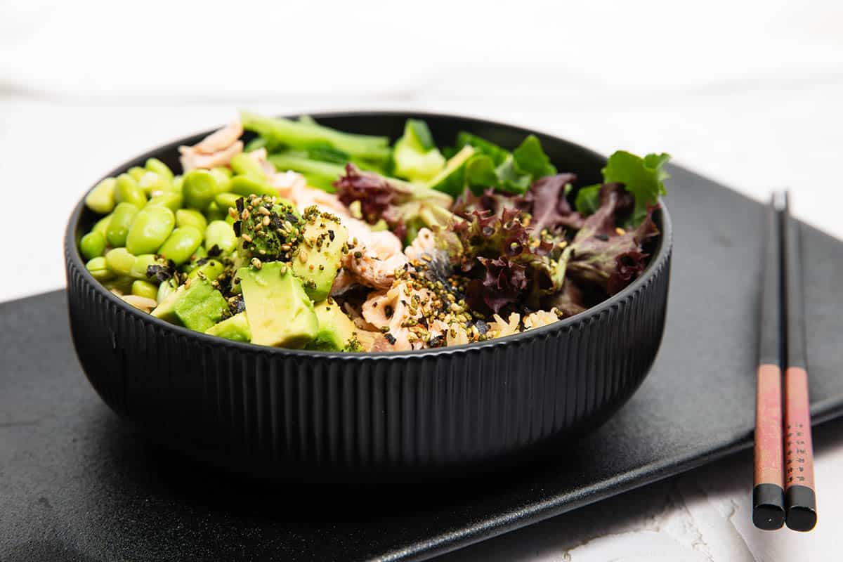 Thermomix Teriyaki Salmon bowl with edamame beans lettuce and advocado sitting on rice in a black bowl.