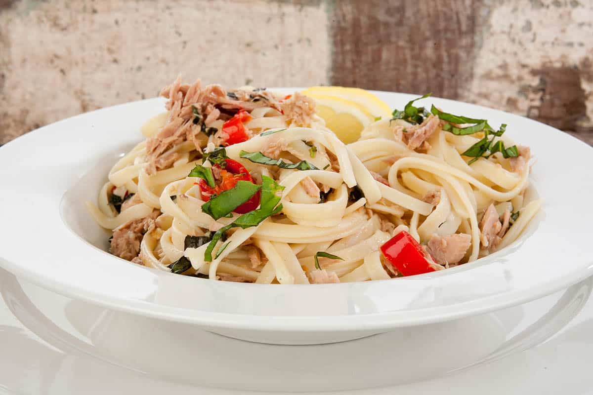 A bowl of tuna linguine  with a wooden background