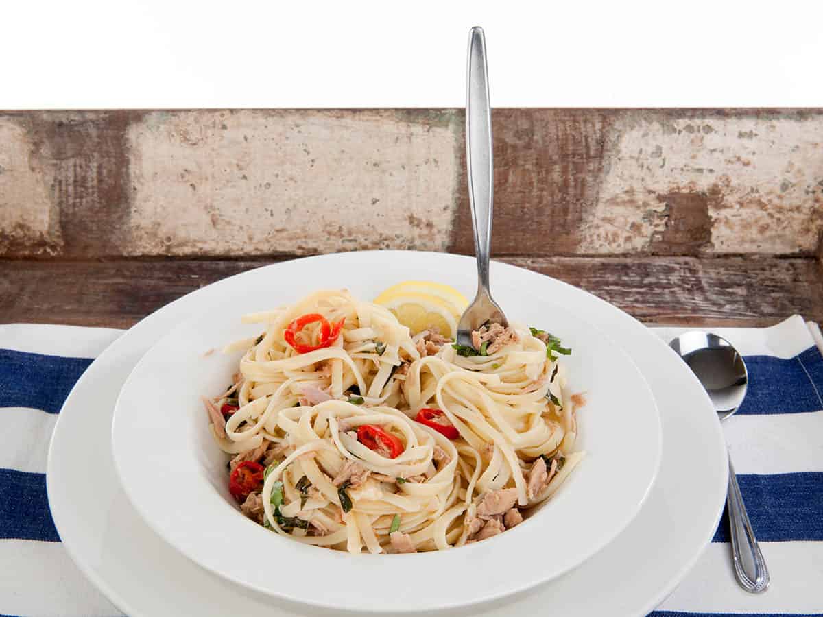 Themomix Tuna linguine in a bowl with a fork on a striped background