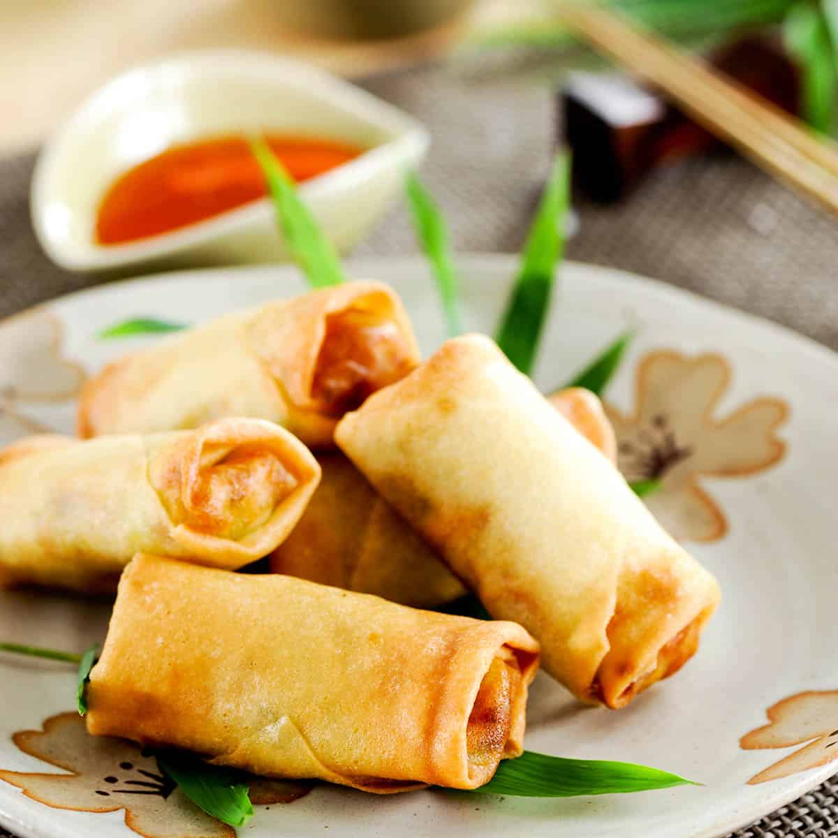 Square image of Thai spring rolls on a floral plate with a dipping sauce