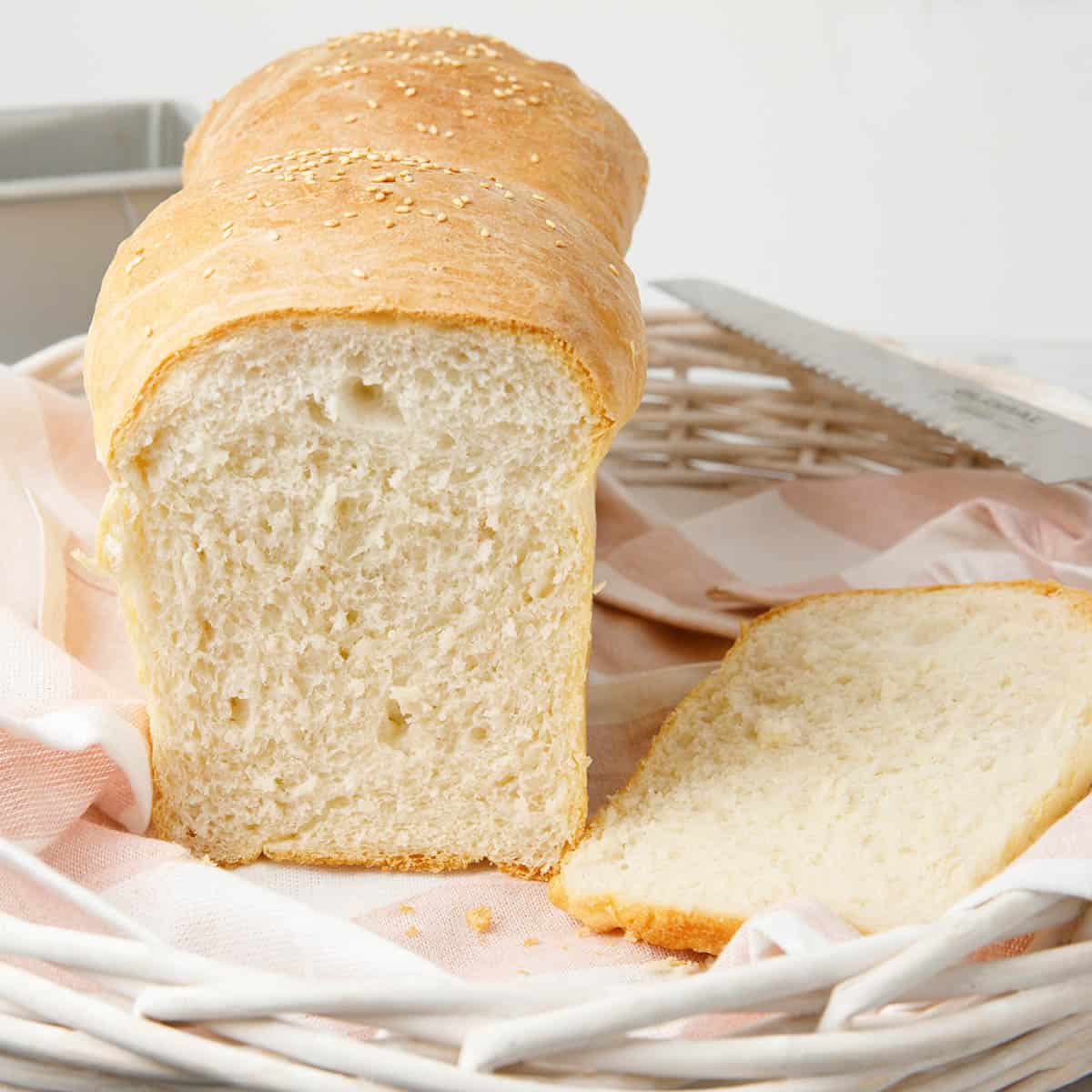 Thermomix Bread Recipe sliced on a tea towel and showing a white basket and bread tin in the background.
