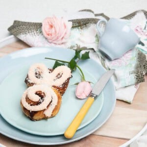 Pink iced cinnamon scroll Easter Bunny made in the Thermomix on a pastel plate background.