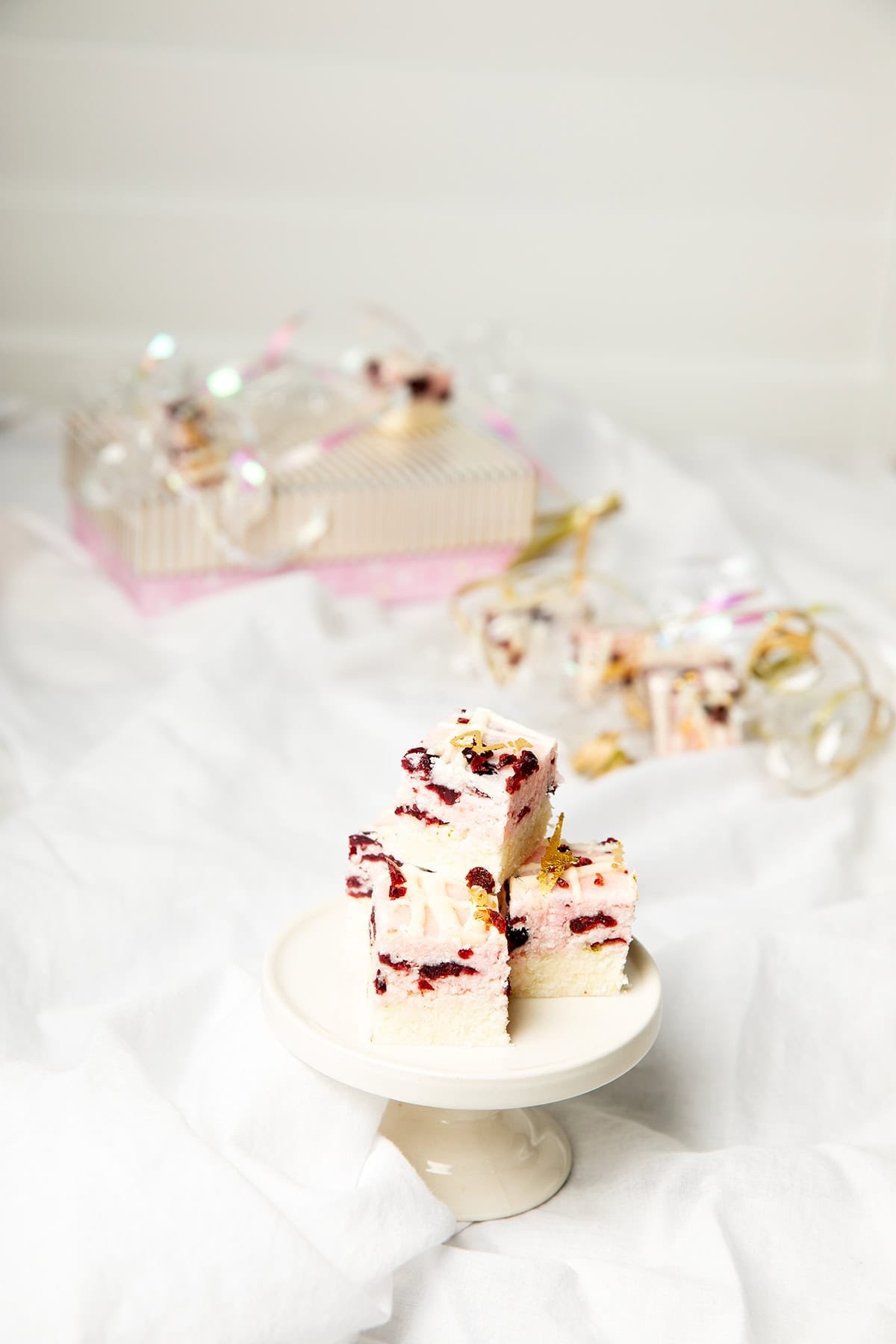Portrait image cranberry and lime coconut ice on a small white platter. Background is white, more coconut ice in the background