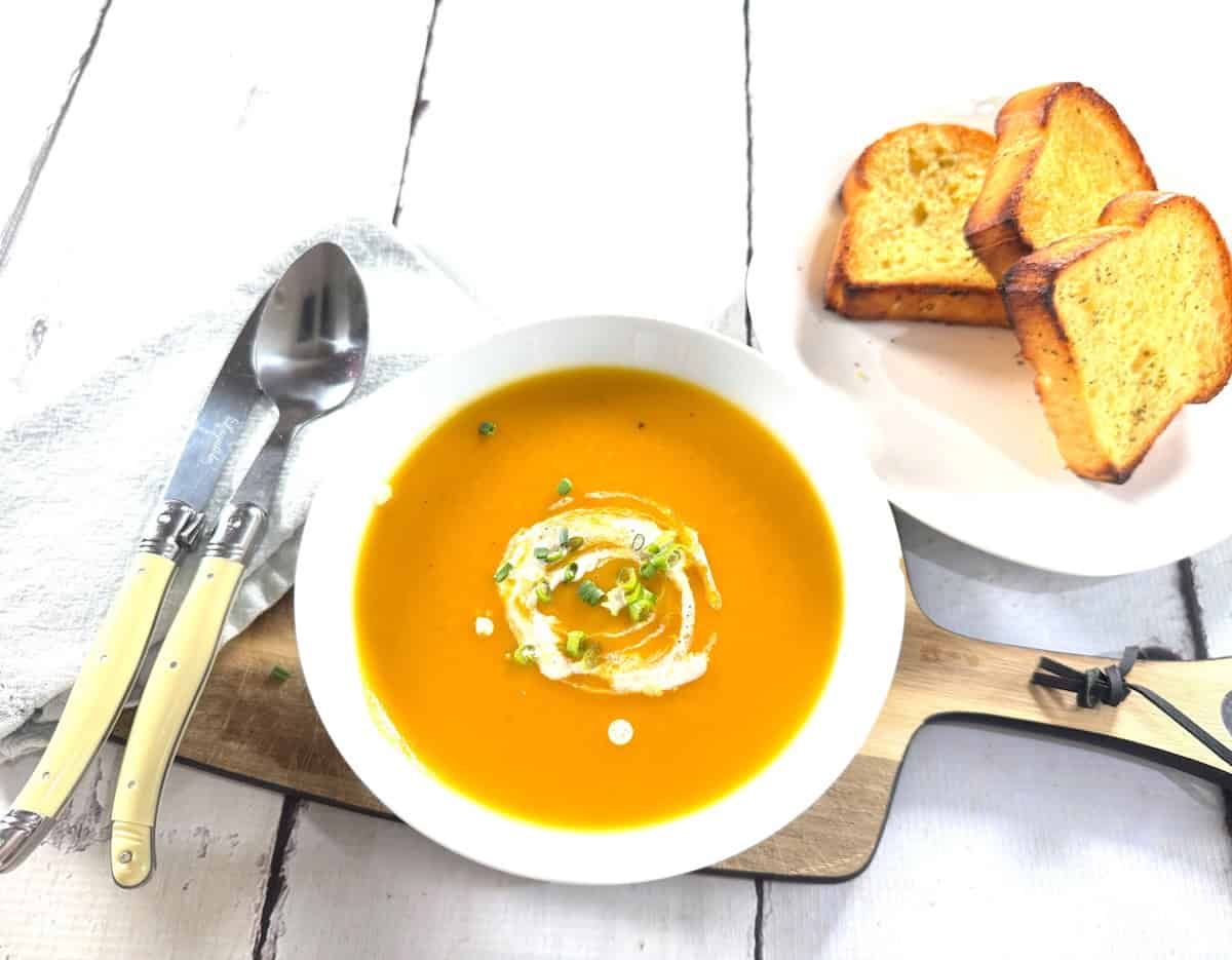 The best ever creamy Thermomix pumpkin soup without heavy cream, served in a bowl with buttered toast and a white background